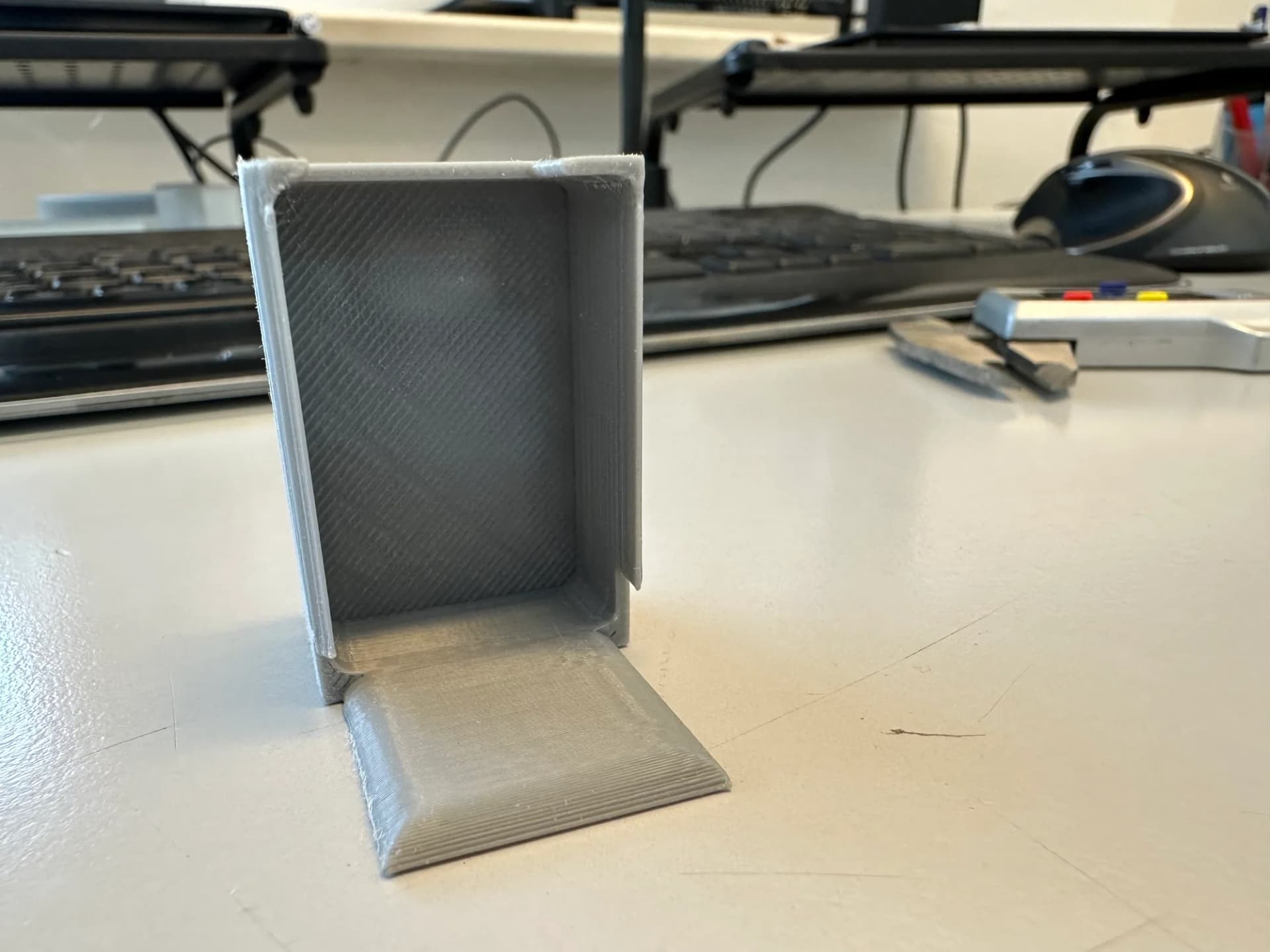 3D-gedruckter grauer Halter mit sichtbaren FDM-Schichtlinien, aufgestellt auf einem Schreibtisch in der elbe3D-Werkstatt