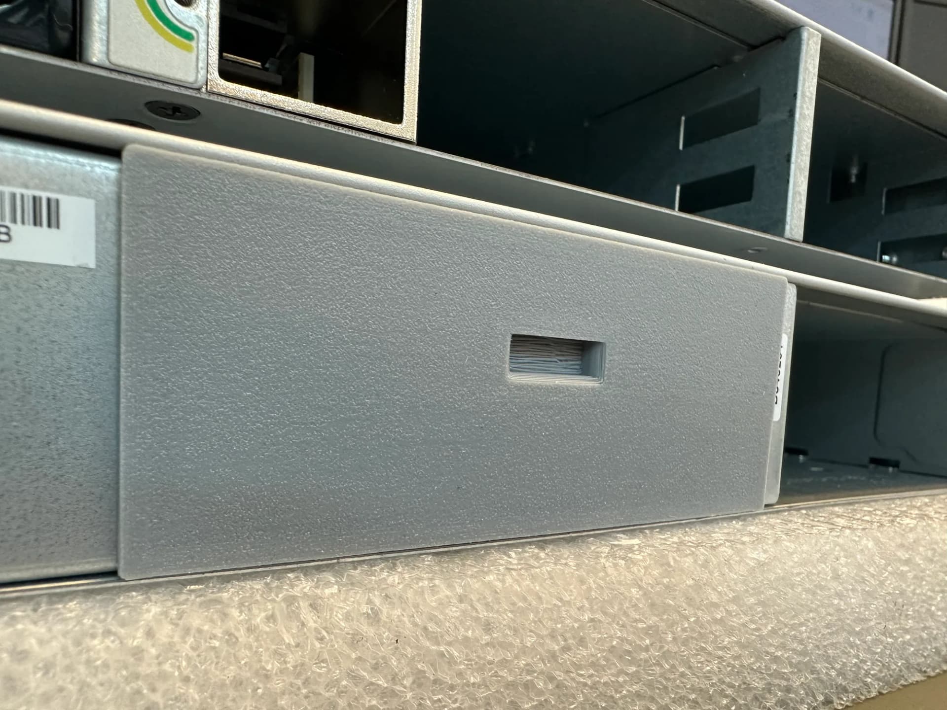 Nahaufnahme einer 3D-gedruckten grauen Blende, eingebaut im Slot eines Netzwerk-Switches